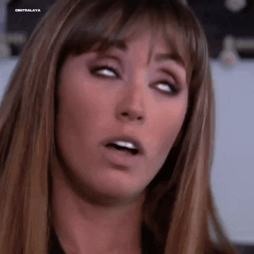 a woman with long hair and bangs is making a funny face with her eyes closed .