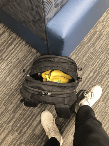 a person is standing next to a black backpack with bananas in it