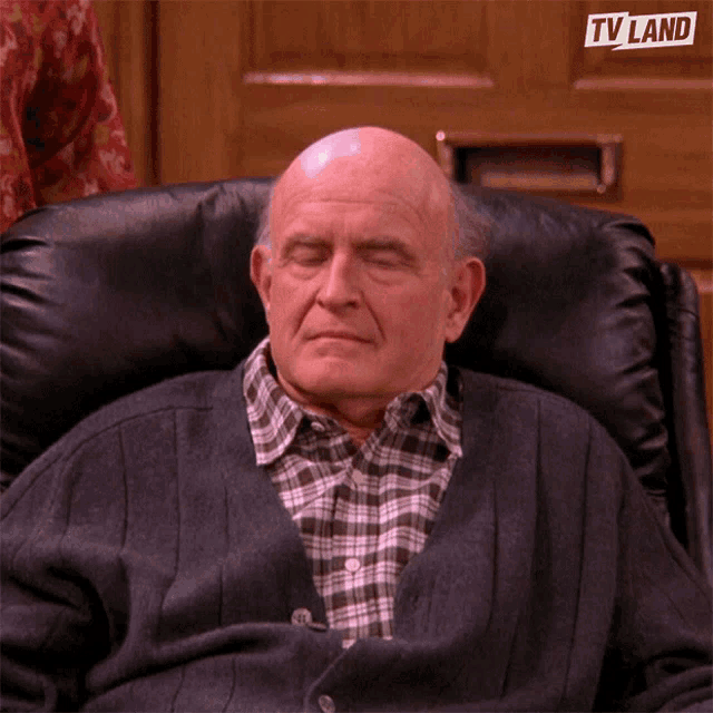 an older man is sitting in a chair with his eyes closed and a tv land logo above his head