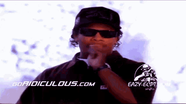 a man wearing sunglasses and a hat is standing in front of a sign that says eazy-ecpt .