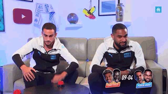 two men are sitting on a couch and one of them has the number 09-04 on his chest