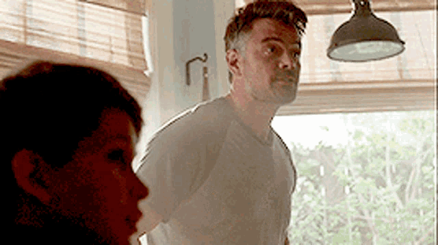 a man and a woman are standing in front of a window in a kitchen .