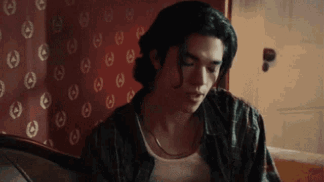 a man with long hair is sitting in front of a wall with a pattern of circles on it