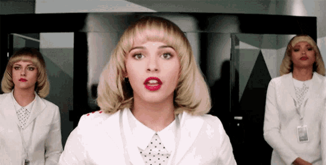 a woman with blonde hair and red lipstick stands in front of two other women in white suits