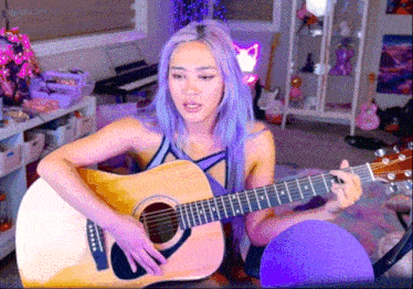 a woman with purple hair is playing a guitar