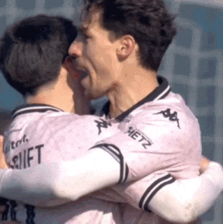 two men in pink jerseys are hugging each other on a soccer field .