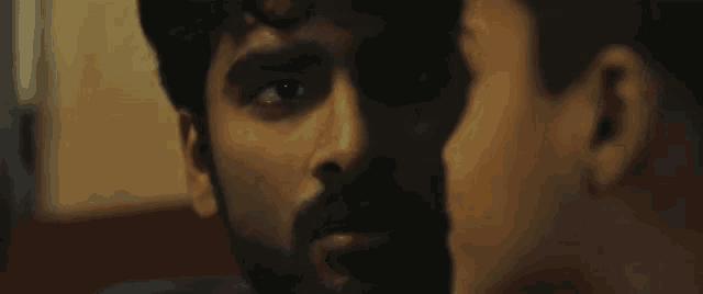 a man with a beard is talking to another man in a dark room with a caption in hindi .