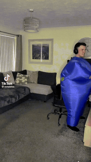 a man in a blue inflatable costume stands in a living room