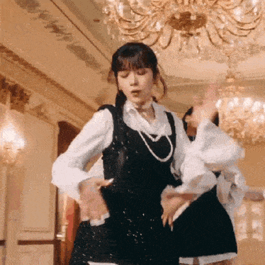 a woman in a black dress and white shirt is dancing in a room with a chandelier .