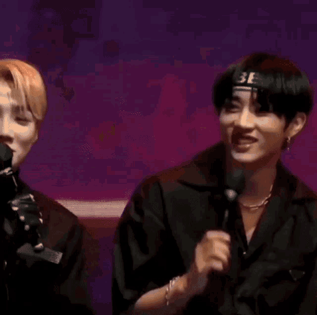 a man wearing a headband is talking into a microphone while another man watches .