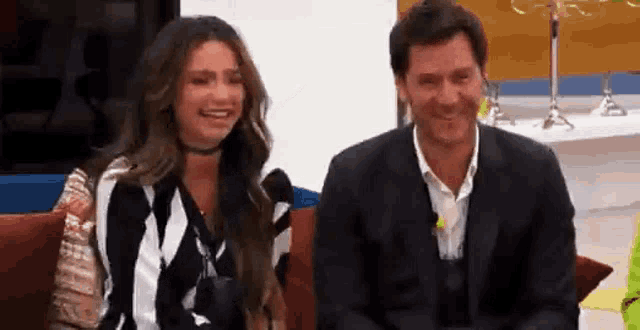 a man and a woman are sitting next to each other on a couch and laughing .