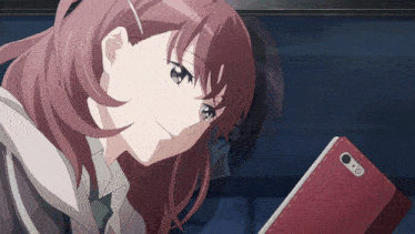a girl with red hair is looking at a red cell phone