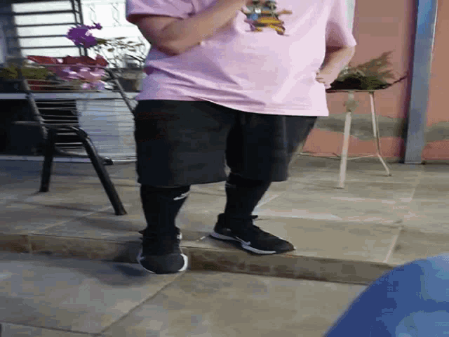 a person wearing a pink shirt and black shorts standing on a sidewalk