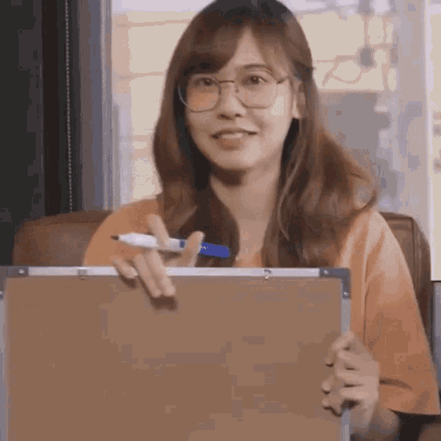 a woman wearing glasses is sitting in a chair holding a marker and a board .