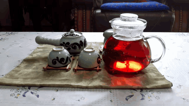 a glass teapot filled with red liquid sits on a table next to three cups