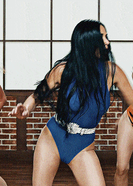 a woman in a blue bodysuit is dancing in front of a window