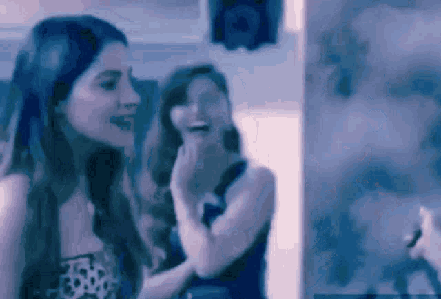 two women are standing next to each other in a dark room laughing .