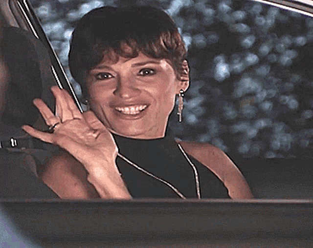 a woman in a black turtleneck is smiling while sitting in a car