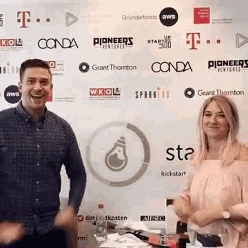 a man and a woman are standing in front of a wall with a lot of logos on it