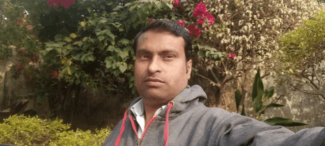 a man in a grey hoodie takes a selfie in front of flowers