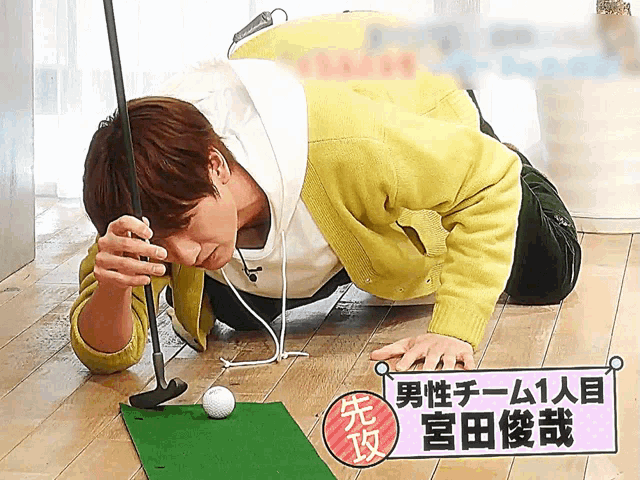 a man kneeling on the floor holding a golf club and a golf ball