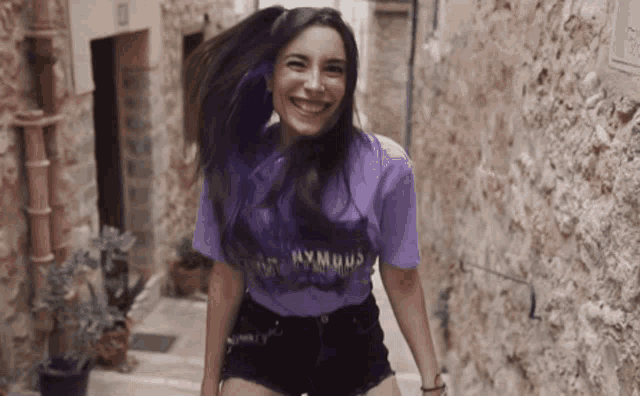 a woman wearing a purple shirt and black shorts smiles