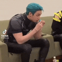 a man with blue hair is sitting on a couch and eating a lollipop .