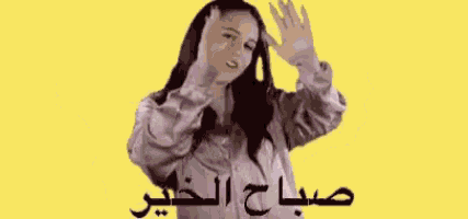 a woman in a purple jacket is waving her hands in front of a yellow background with arabic writing .