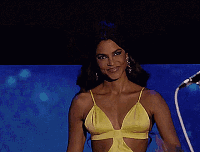 a woman in a yellow dress smiles and holds her hand to her chest
