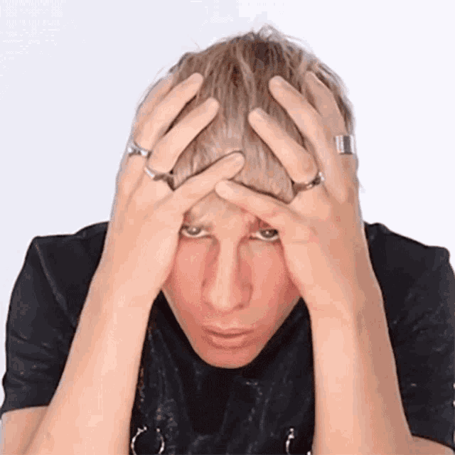 a man with rings on his hands holds his head