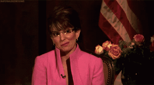 a woman in a pink suit is smiling and says `` you 're welcome '' in front of an american flag .