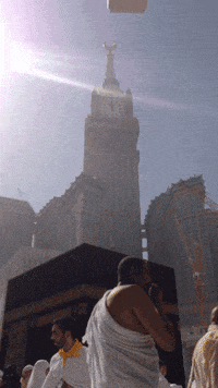 a man in a white robe stands in front of a large building with a clock tower in the background