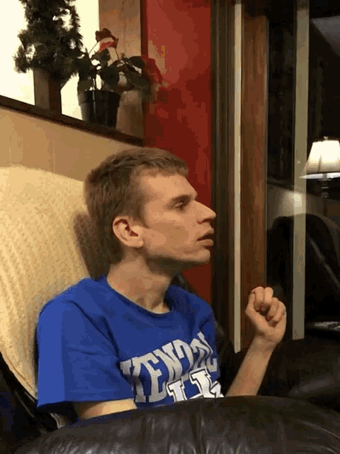 a man wearing a blue shirt that says tennessee on it sits on a couch