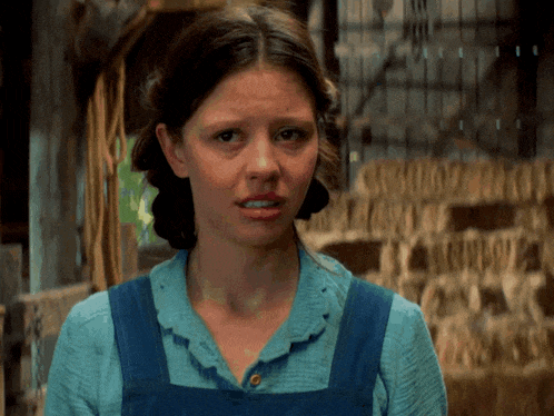 a woman in a blue shirt and blue overalls is making a face