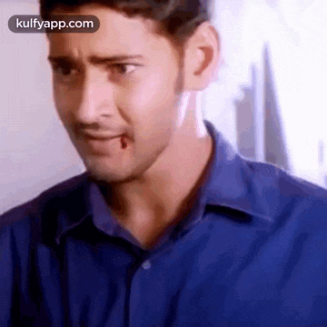a man in a blue shirt is making a funny face with a bug in his mouth .