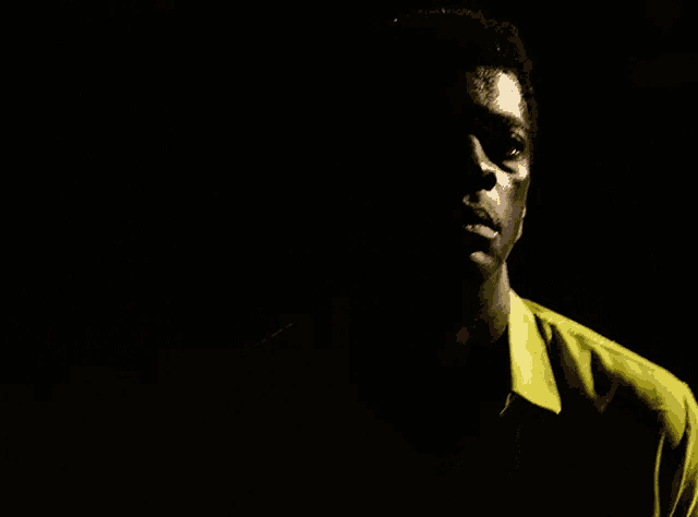 a man in a yellow shirt is standing in a dark room