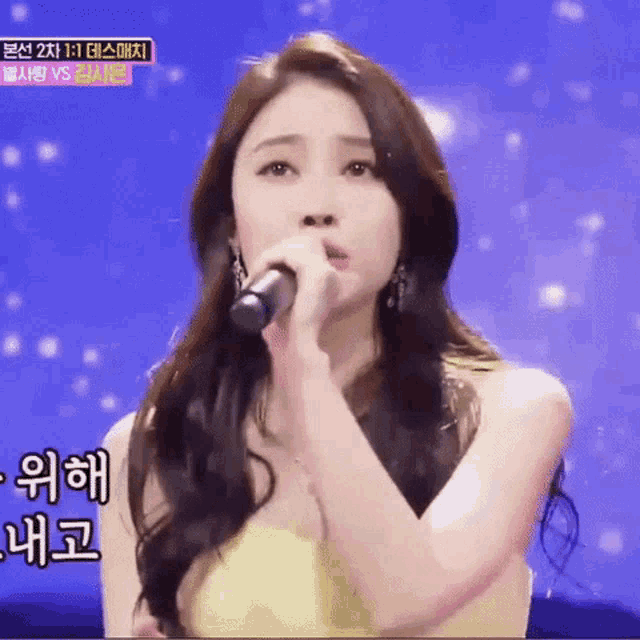 a woman is singing into a microphone while wearing a yellow dress and earrings .