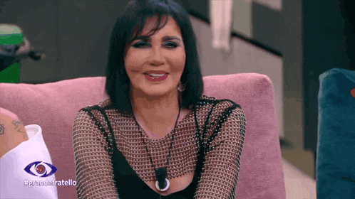 a woman sits on a pink couch with a big eye behind her that says #grandetratello
