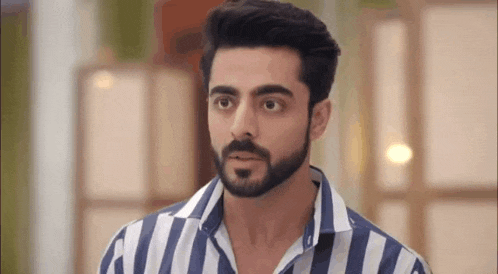 a man with a beard and a striped shirt is standing in a room .