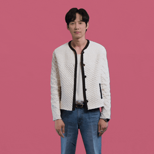 a man wearing a white sweater and blue jeans is standing in front of a pink background