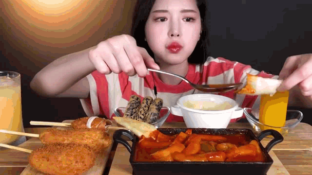 a woman is eating food with a spoon and a glass of orange juice in the background