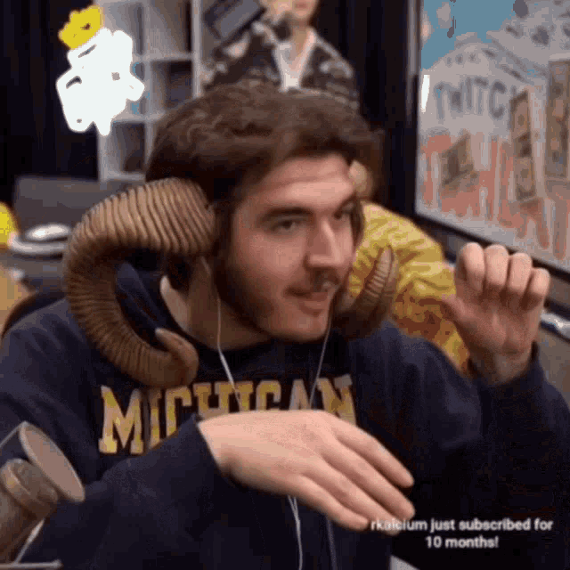 a man wearing a michigan sweatshirt has a fake ram 's horns on his head