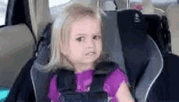 a little girl is sitting in a car seat and looking at the camera .