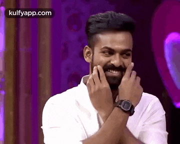 a man with a beard is wearing a watch and smiling while covering his face with his hands .