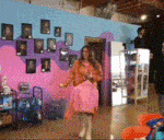 a woman in a pink dress is standing in front of a wall with pictures of people on it