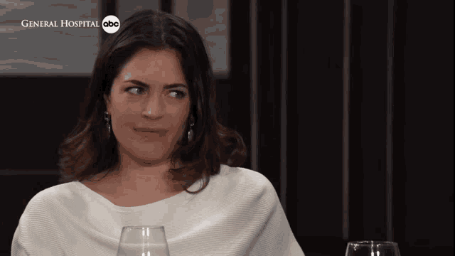a woman is sitting at a table with a glass of wine in front of a sign that says general hospital abc