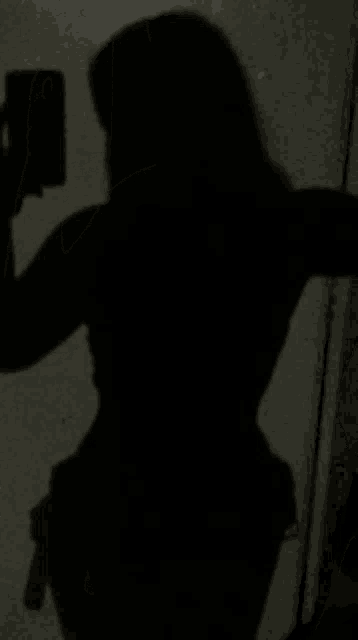 a shadow of a woman taking a selfie with her cell phone in front of a mirror .