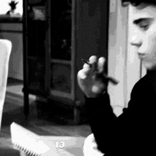 a black and white photo of a man smoking a cigarette in a living room .
