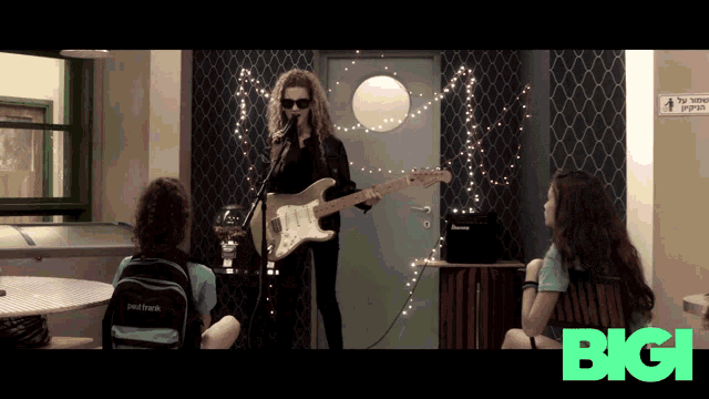 a woman singing into a microphone while playing a guitar with the bigi logo in the corner