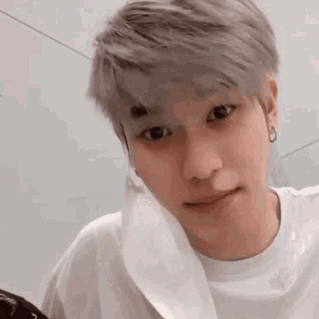 a young man with gray hair is wearing a white shirt and earrings and looking at the camera .